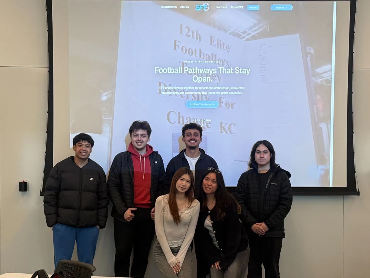 The six-person Elite Footballers Tournament project team standing in front of a projection of the operational website.